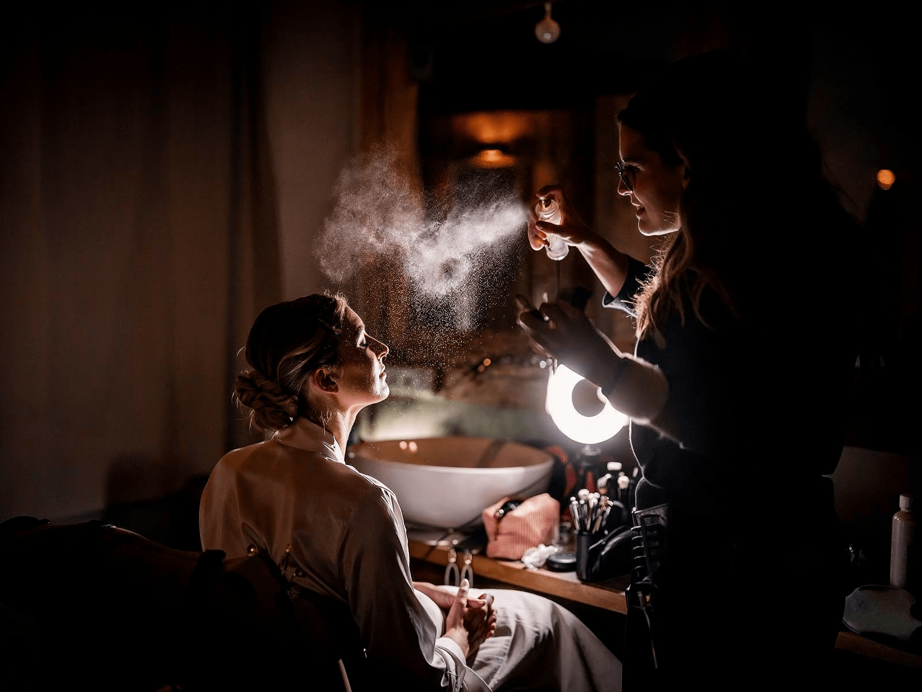 A makeup artist setting a woman’s makeup with a fine mist